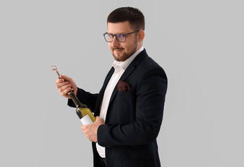 Young sommelier opening bottle of wine on grey background