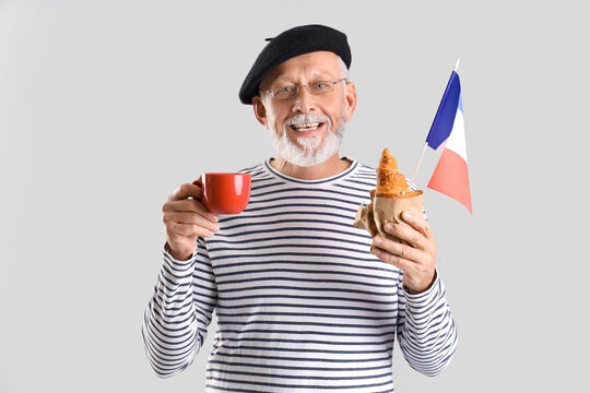 Senior man with flag of France, coffee cup and croissant on light background - Powered by Adobe