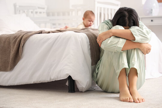Young woman with her baby suffering from postnatal depression in bedroom - Powered by Adobe