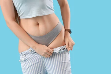 Zelfklevend Fotobehang Young woman in tight jeans on blue background, closeup. Weight gain concept © Pixel-Shot