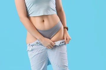 Foto op Canvas Young woman in tight jeans on blue background, closeup. Weight gain concept © Pixel-Shot