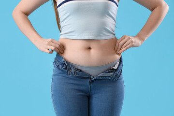 Fototapeta premium Young woman in tight jeans on blue background, closeup. Weight gain concept