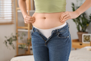 Fototapeta premium Young woman in tight jeans at home, closeup. Weight gain concept