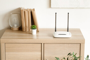 Modern wi-fi router with books, plant and lamp on commode in room