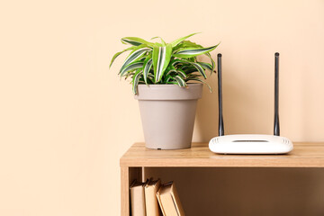 Modern wi-fi router with plant on shelf near beige wall