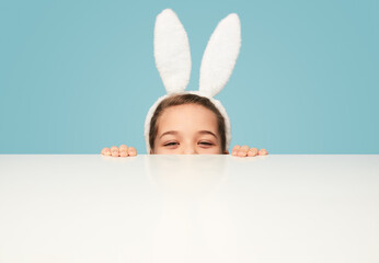 Playful girl in bunny ears hiding behind table
