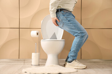 Young man with hemorrhoids and thumbtack on toilet bowl in restroom - obrazy, fototapety, plakaty
