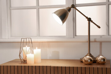 Burning candles with golden lamp on commode in room at night