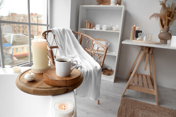 Burning candles with coffee cup on bathtub in light room, closeup