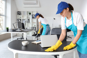 Female janitor cleaning table in office - obrazy, fototapety, plakaty
