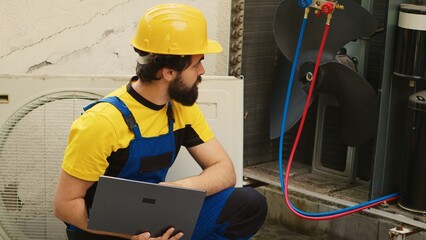 Licensed serviceman using laptop to look online for new evaporator coil after finding external HVAC...