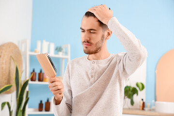 Young man with hair loss problem and brush in bathroom