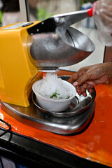 The ice is being shaved using a shaved ice machine into a white bowl