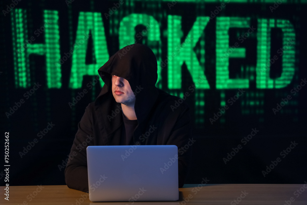 Poster hacker with laptop at table against word hacked on dark background