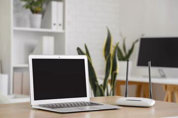 Modern wi-fi router with blank laptop on table in office