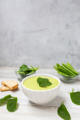 Homemade spinach cream soup in white bowl with bread on white wooden background. 