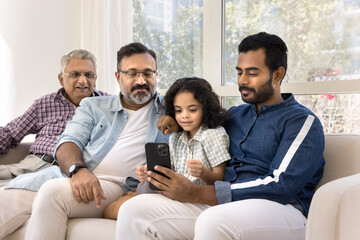 Focused Indian relatives of four different family generations using online application, media...