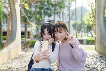 Two young Taiwanese female college students are sitting happily talking on the university campus in Taipei, Taiwan. 台湾台北の大学キャンパスで二人の若い台湾人女性の大学生が楽しそうに話しながら座っている