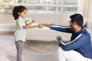 Positive strong Indian dad training little daughter kid, teaching boxing, showing fist work. Cute girl and young father exercising at home together, learning martial arts, fighting
