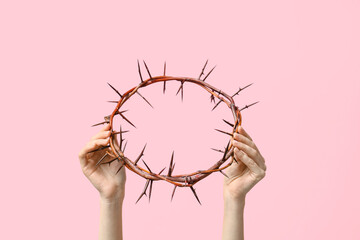 Female hands with crown of thorns on pink background, closeup. Good Friday concept