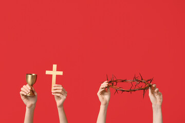 Female hands with crown of thorns, cup and cross on red background. Good Friday concept