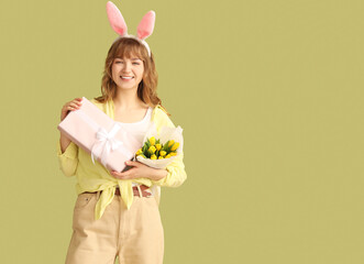 Young girl with Easter bunny ears, flowers and gift on color background