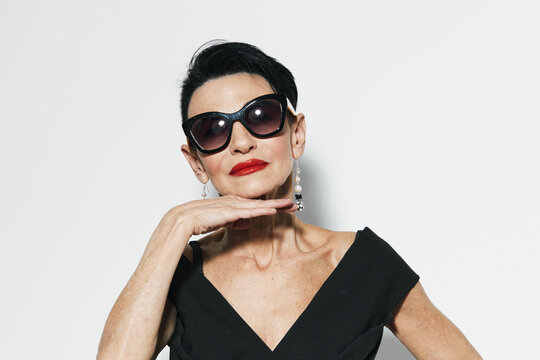 Stylish woman in black dress and sunglasses posing confidently for the camera with hand on chin