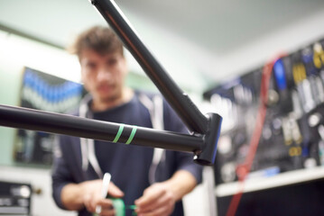 Process of preparing a bicycle frame with masking tape for a custom painting design in a workshop. Selective focus composition.