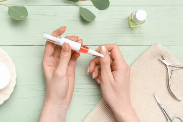 Female hands applying cuticle oil onto fingernails, eucalyptus twig and towel on green wooden...