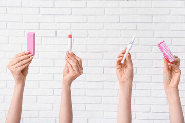 Female hands with cuticle oil pens, nail buffer and brush on white brick background