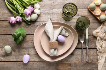 Table setting for Easter celebration with green bunny toy and painted eggs on wooden background. Top view