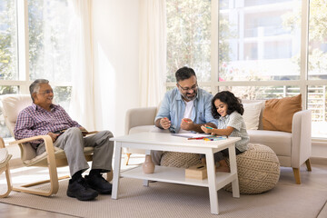 Happy Indian grandpa and cute granddaughter girl drawing in paper album together, enjoying art,...