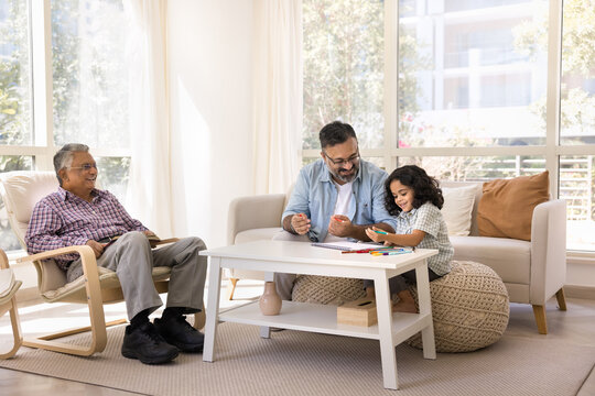 Happy Indian grandpa and cute granddaughter girl drawing in paper album together, enjoying art, creative, hobby, leisure time, doing school homework. Two grandfathers watching child