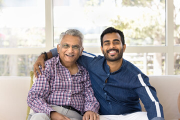 Positive adult Indian grandson embracing elderly grandad, giving family support, looking at camera...