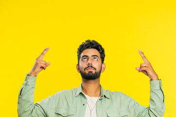 Indian bearded man showing thumbs up and pointing overhead, above head empty place, advertising area for commercial text copy space for goods promotion advertisement. Guy isolated on yellow background