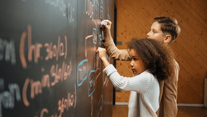 Diverse student brainstorm engineering prompt on blackboard. Group of happy children helping,...