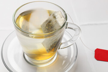 Tea bag in cup with hot drink on white table, closeup