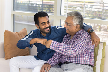 Happy joyful Indian young adult child man and senior father making fist bump friends gesture,...