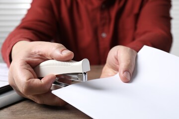 Man stapling papers at wooden table, closeup