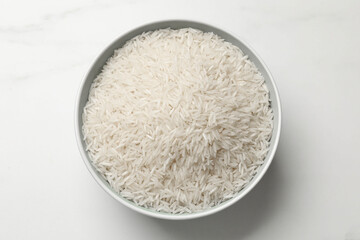 Raw basmati rice in bowl on white table, top view