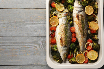 Delicious fish with vegetables and lemon in baking dish on grey wooden table, top view. Space for text