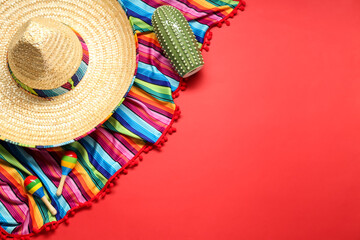 Mexican sombrero hat, toy cactus and colorful poncho on red background, flat lay. Space for text