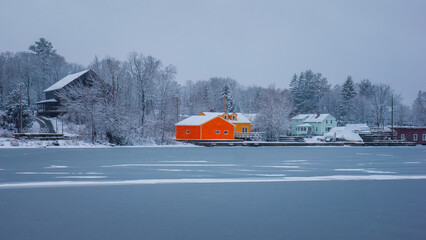 A winter landscape of a frozen Moosehead Lake with colorful orange houses on its shore, under a heavy snowfall. Greenville, Maine, US