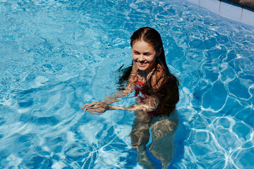 Happy woman swimming in the pool in red swimsuit with loose long hair in the sunshine, skin protection with sunscreen, concept of relaxing on vacation.