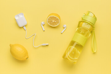 A sports bottle with water and lemon and wireless headphones on a yellow background.