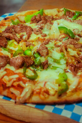 flank steak pizza with peppers, onion and extra gratin cheese Mexican style on a wooden platform in a restaurant