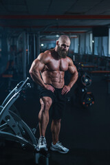 Fototapeta na wymiar Muscular bald man posing in shorts. Bodybuilder showing off his shape in the gym. 