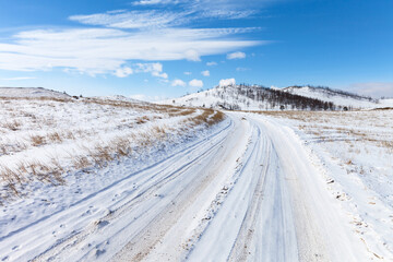 Fototapeta na wymiar Snowy dirt road on Teheran steppe to Baikal Lake coast on sunny cold February day. Beautiful winter landscape. Natural background. Winter travels and outdoor recreation