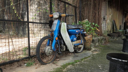 An older blue motorcycle abandon next to a rustic building