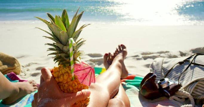 Legs, person and relaxing at beach with drink, peaceful and pov at tropical destination or holiday. Resting, fruit cocktail and calming waves by paradise, nature and wellness for travel in outdoors
